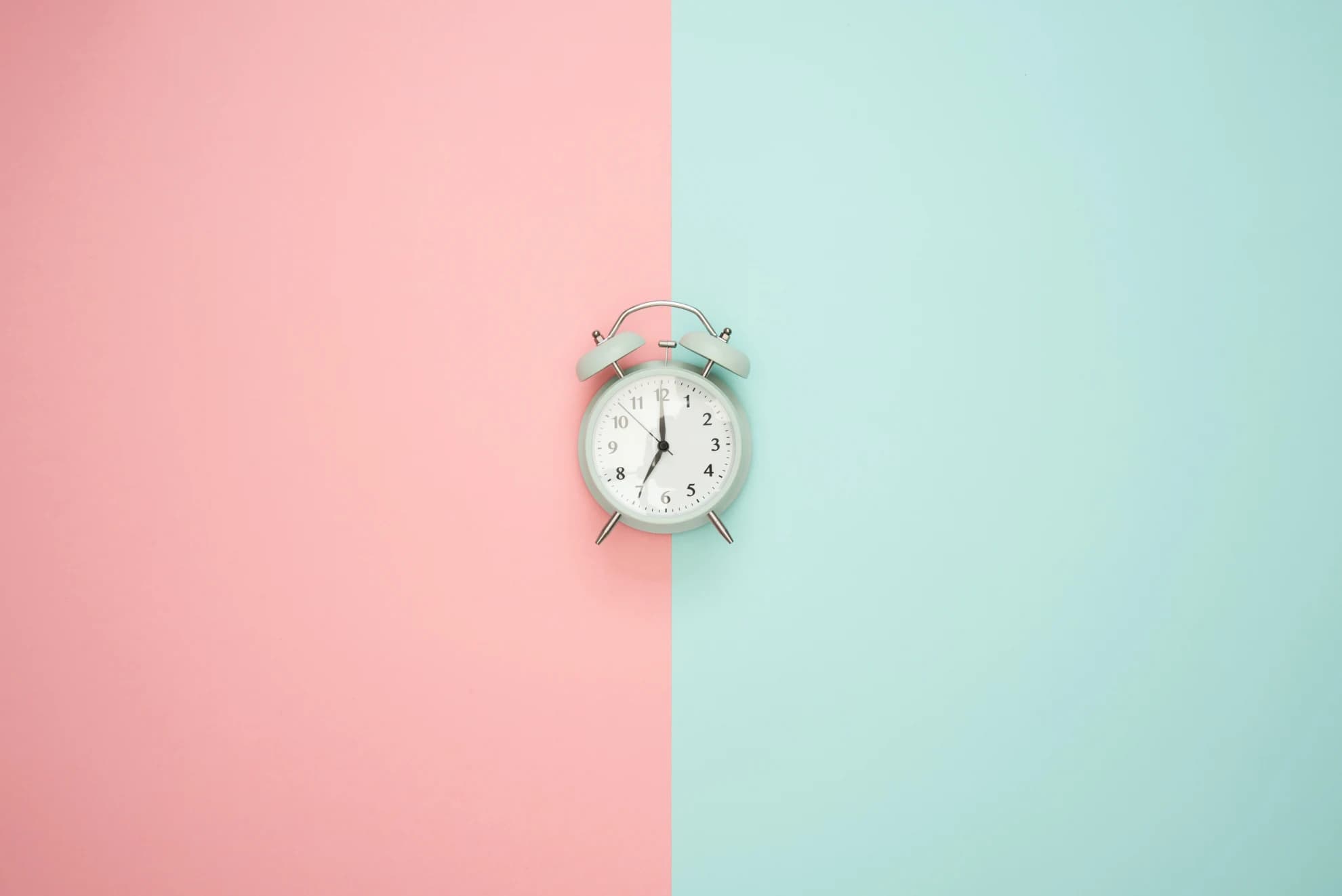 A white, old-school alarm clock in the middle of a dual-toned pink (left) and blue (right) image to signify what @thinkjrs could quickly find that visually represented the program 'cron'.