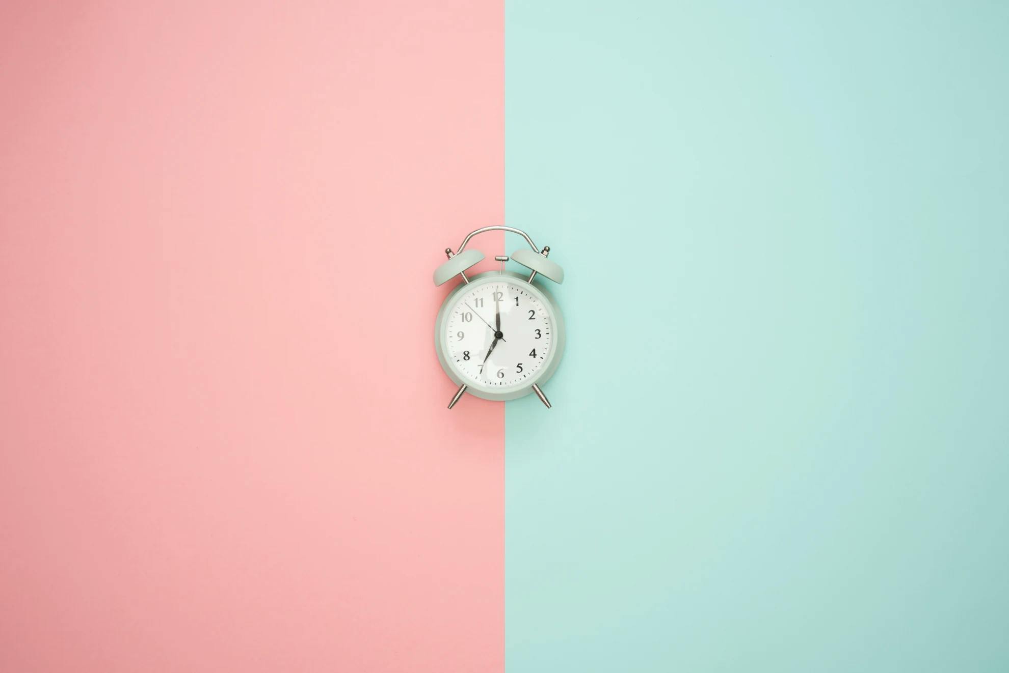 A white, old-school alarm clock in the middle of a dual-toned pink (left) and blue (right) image to signify what @thinkjrs could quickly find that visually represented the program 'cron'.